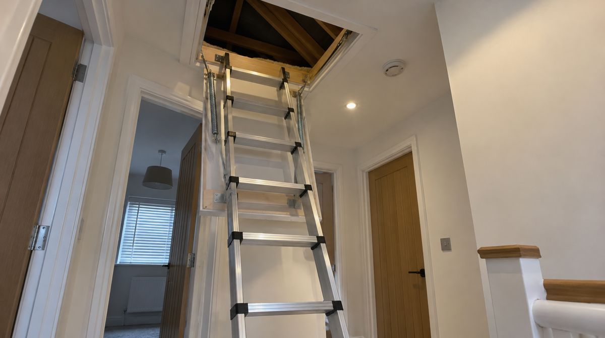 Aluminium folding loft ladder pulled down from an insulated hatch on an upstairs landing