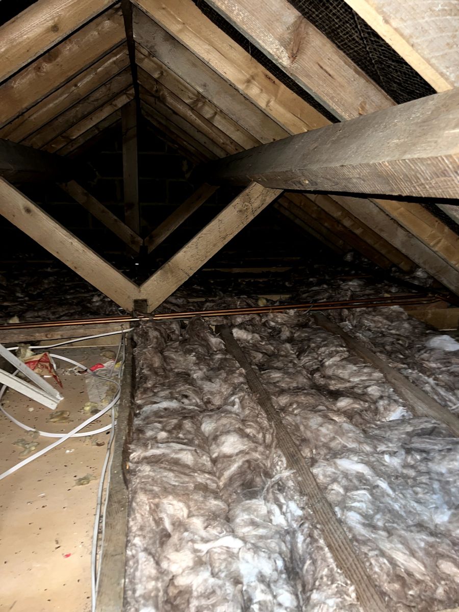 Mineral wool insulation between the joists of an older loft with pipework and timber purlins