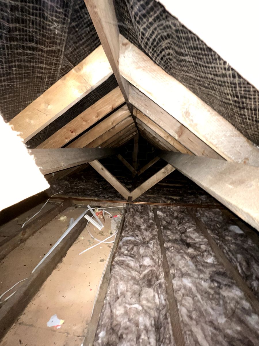 Fresh mineral wool insulation laid between joists in an older cut-roof loft, next to a boarded strip