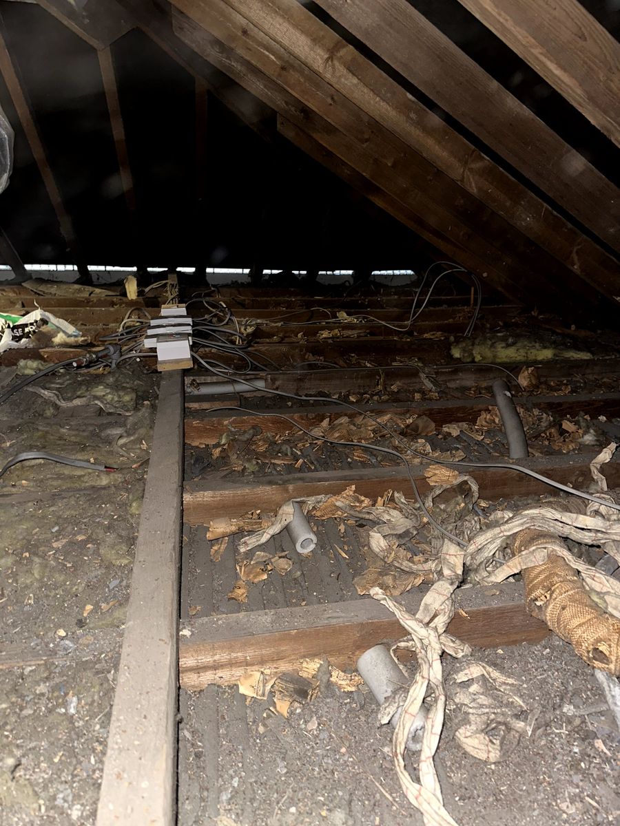 Older loft before work, with debris, old lagging, loose cables and little insulation between the joists